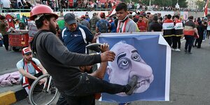 EIn Mann tritt mit dem Fuß gegen ein Plakat, das das Gesicht eines Mannes zeigt.