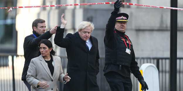 Boris Johnson und Begleitung gehen durchPolizei-Absperrband nach dem Terror
