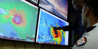 Mitglieder eines Katastrophenteams schauen auf Monitore mit Bildern eines Hurrikans