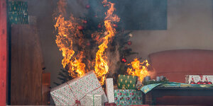 ein brennender Weihnachtsbaum, davor eingepackte Geschenke
