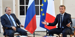 Putinund Macron sitzen vor Flaggen