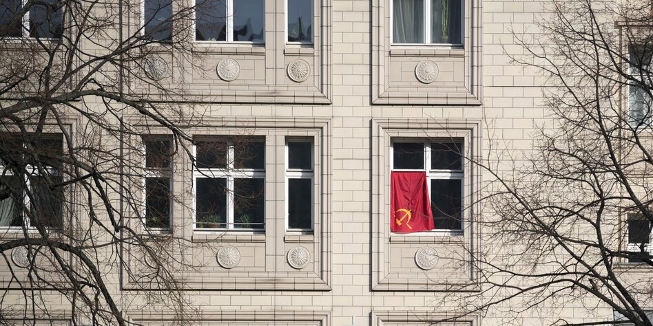 Rote Fahne mit Symbol Hammer und Sichel an der Fassade von Wohnhaus an der Karl-Marx-Allee in Berlin Friedrichshain.