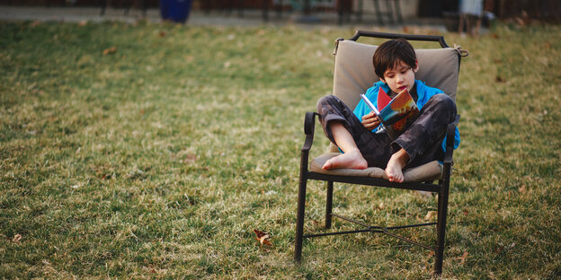Ein Kind sitzt auf einem Stuhl und liest in einem Buch