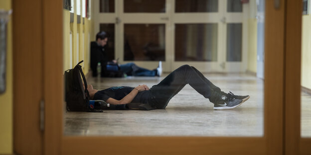 Ein Schüler liegt in einem Gang im Stefan-George-Gymnasium auf dem Boden.