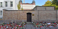 Vor der Mauer einer Synagoge liegen rechts und links neben der Tür Kerzen und Blumen