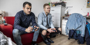 Zwei junge Männer auf der Couch spielen Playstation Zwei junge Männer auf der Couch spielen Playstation