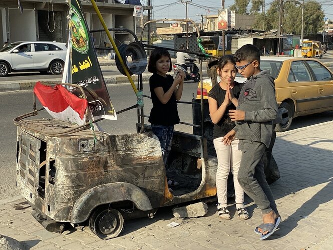 Kinder stehen vor einem ausgebrannten Tuktuk