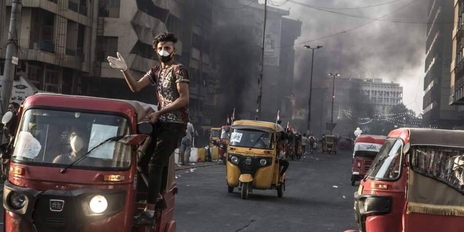 Ein Mann lehnt sich aus einem fahrenden Tuktuk durch eine Straße, in der es brennt