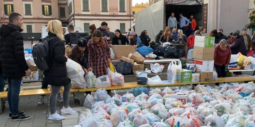 Im Vordergrund reihen sich viele volle Tüten, hinten werden sie auf einen LKW verladen