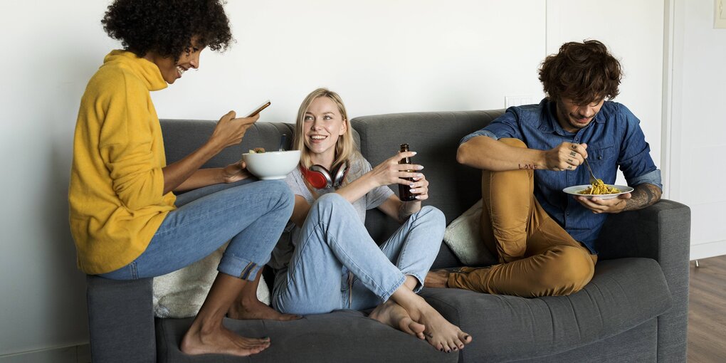 2 frauen und 1 Mann auf dem Sofa mit Essen und Bier