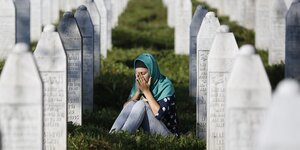Eine Frau sitzt zwischen Grabsteinen und hält sich die Hände vor ihr Gesicht