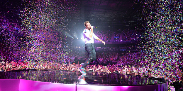 Der Sänger Chris Martin von Coldplay auf der Bühne, umgeben von Fans und phanatstischer Deko die