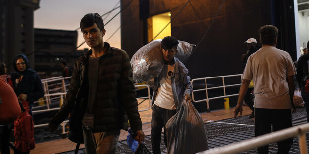 Zwei junge Männer verlassen ein Schiff mit schweren paketen auf dem Rücken