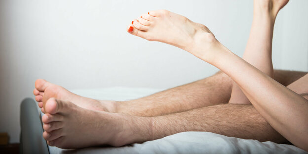 Zwei Frauen- und zwei Männerbeine beim Füßeln im Bett