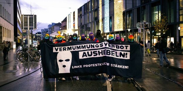 Hinter einem Banner mit der Aufschrift "Vermummungsverbot aushebeln, linke Protestkultur stärken" stehen vermummte Menschen