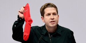 Kevin Kühnert steht am Rednerpult und hält eine rote Socke in der Hand