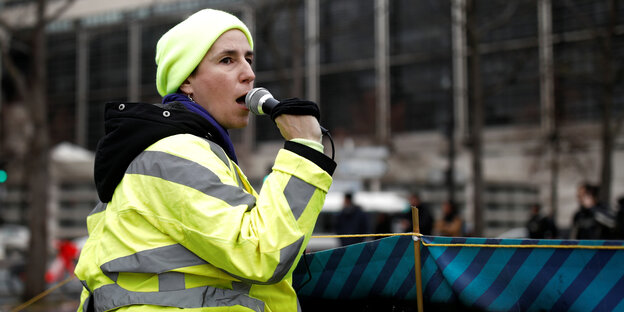 Sophie Tissier ruft in ein Mikrofon. Die junge Frau trägt eine gelbe Warnweste und eine gelbe Mütze.