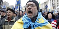Ein Mann ruft etwas und hat sich die Fahne der Ukraine umgehängt