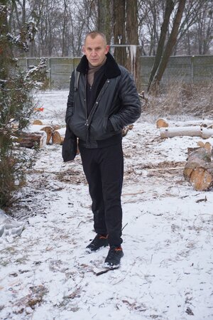 Ein Mann in schwarzer Lederjacke steht in einem schneebedeckten Hof Ein Mann in schwarzer Lederjacke steht in einem schneebedeckten Hof