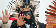 Ein indigener Klimaaktivist mit Federschmuck und schwarzer Gesichtsbemalung hält seine Hand in die Kamera