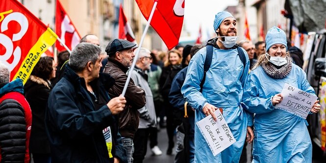 ein Mann und eine Frau in blauer Verkleidung gehen an Menschen vorbei, die Gewerkschaftsfahnen tragen