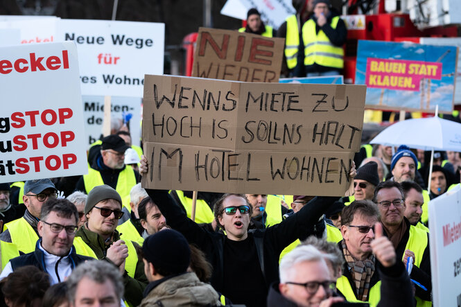 Demonstration mit Schildern, auf einem steht: Wenns Miete zu hoch is, sollns halt im Hotel wohnen.