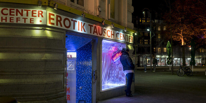 Eine Frau steht an einer Straßenecke unter einem Schild, auf dem steht: "Erotik Tausch Center"