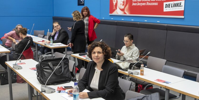 Amira Mohamed Ali, die neue Fraktionsvorsitzende der Linken, sitzt an einem Schreibtisch, im Hintergrund ein Plakat der Partei die Linke