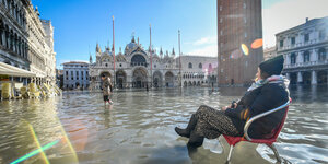 Eine Frau sitzt in Venedig auf einem Stuhl im Hochwasser auf dem Markusplatz.