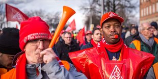 Männer haben Tröten und Trillerpfeifen und sind in rote Plastikumhänge und Warnwesten gekleidet