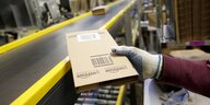 Eine Hand nimmt ein Paket der Firma Amazon von einem Fliessband