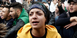 Ein Mensch in gelber Kapuzenjacke weint, während er mit anderen demonstriert.