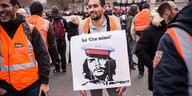 Ein Demonstarnt trägt ein Plakat auf dem Che Guevara mit einer Eisenbahnmütze zu sehen ist