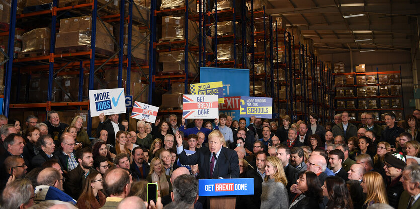 Premier Boris Johnson spricht im Rahmen einer Wahlkampfveranstaltung zur Menge. Einzelne halten Schilder zum Thema Brexit hoch.