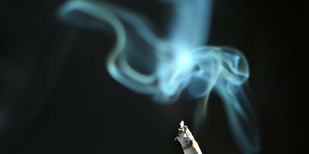 eine glimmende Zigarette und Rauchschwaden vor schwarzem Hintergrund