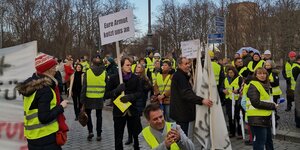 Unterschriftensammlung und Demo: Menschen protestieren in gelben Westen, einer hält ein Schild hoch, auf dem steht: "Eure Armut kotzt uns an"