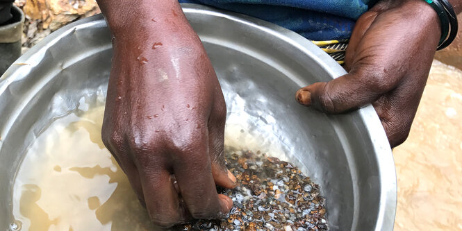 Hände wühlen in einer Schüssel mit Wasser und Steinbröseln