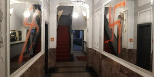 Ein Hausflur mit zwei Wandspiegeln links und rechts. Darauf mit rotem Grafitti jeweils eine große SS-Rune und ein Hakenkreuz geschmiert.