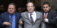 Harvey Weinstein im Anzug, untergehakt von zwei Männern