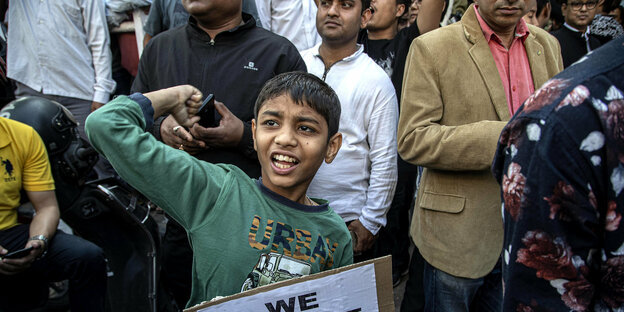 Ein Junge trägt ein Pappschild mit der Aufschrift "We oppose CAB" und reckt seine Faust