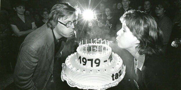 Ein Schwarz-Weiß-Foto, auf dem ein Mann und eine Frau Kerzen auf einer großen Torte auspuste