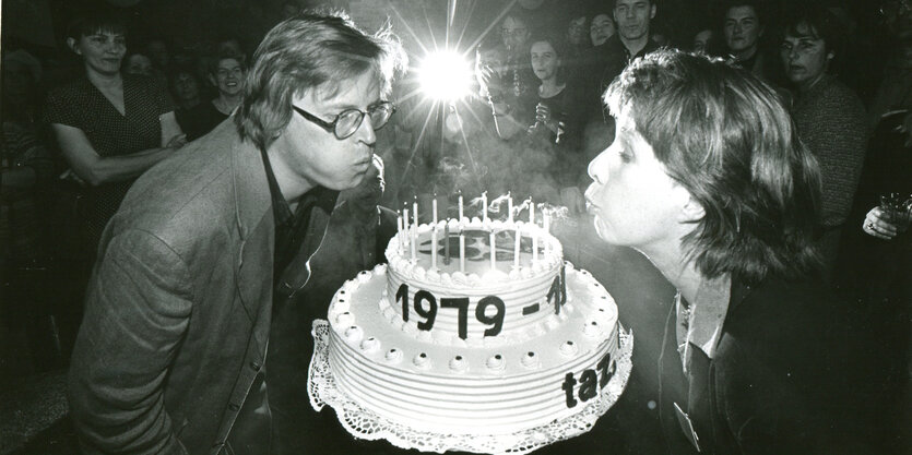 Ein Schwarz-Weiß-Foto, auf dem ein Mann und eine Frau Kerzen auf einer großen Torte auspuste