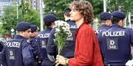 Eine Frau trägt weiße Blumen und geht an einer Reihe von Polizisten vorbei