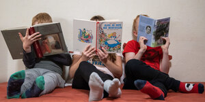 Drei Kinder sitzen auf dem Boden und lesen ein Buch