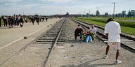 Zwei junge Männer sitzen mit einem Gedenkstrauß auf den Gleisen vor der KZ-Gedenkstätte Auschwitz-Birkenau