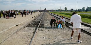 Zwei junge Männer sitzen mit einem Gedenkstrauß auf den Gleisen vor der KZ-Gedenkstätte Auschwitz-Birkenau