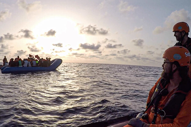 Szene auf dem Meer, gefülltes Rettungsboot weiter hinten, vorne anderes Boot mit Menschen in Rettungswesten