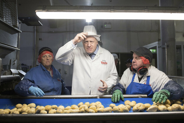 Mann und Frau vor einem Fließband mit Kartoffeln drauf, zwischen ihnen ein Mann in weiß, es ist der britische Premierminister Boris Johnson