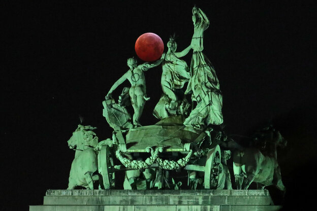 Kupferstatuen bei Nacht, dahinter in der Ferne der sehr rote Mond