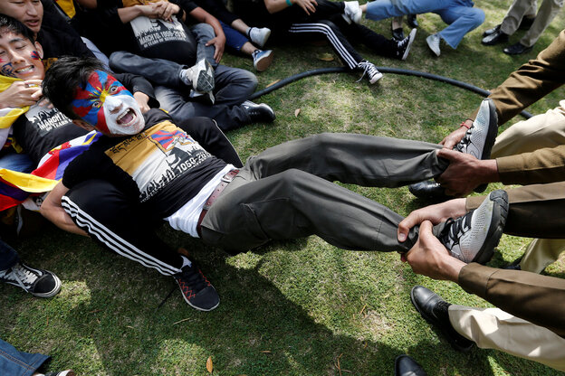 Person mit Tibet-Fahne sitzt auf den Boden, Menschen ziehen an den Beinen, andere halten die Arme fest